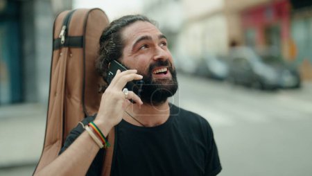 Téléchargez les photos : Jeune homme hispanique musicien parlant sur smartphone tenant étui de guitare à la rue - en image libre de droit