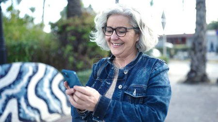 Téléchargez les photos : Middle age woman with grey hair using smartphone at park - en image libre de droit