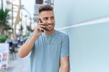Foto de Joven hombre hispano sonriendo confiado hablando en el teléfono inteligente en la calle - Imagen libre de derechos