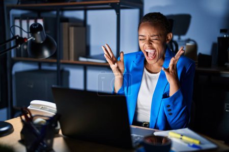 Téléchargez les photos : Belle femme afro-américaine travaillant au bureau la nuit célébrant fou et fou de succès avec les bras levés et les yeux fermés hurlant excité. concept gagnant - en image libre de droit