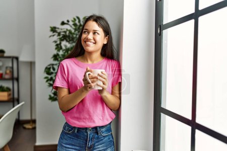 Foto de Joven latina sonriendo confiada bebiendo café en casa - Imagen libre de derechos