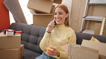 Téléchargez les photos : Young blonde woman talking on smartphone drinking orange juice at new home - en image libre de droit