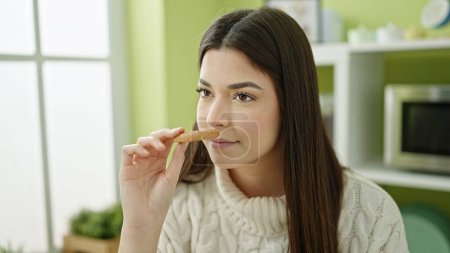 Photo for Young beautiful hispanic woman smelling cookie sitting on table at home - Royalty Free Image