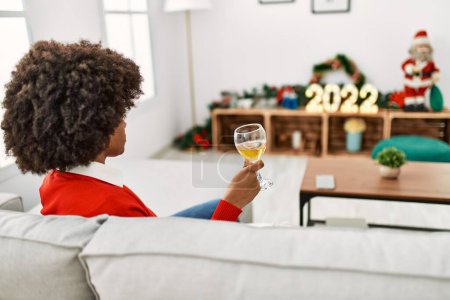 Photo for Young african american woman toasting with wine sitting by christmas decor at home - Royalty Free Image