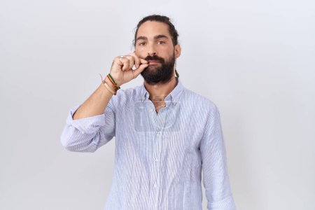 Téléchargez les photos : Homme hispanique avec barbe portant une chemise décontractée bouche et lèvres fermées comme zip avec les doigts. secret et silencieux, tabou parlant - en image libre de droit