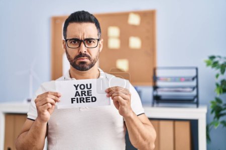 Photo for Young hispanic man with beard holding you are fired banner at the office skeptic and nervous, frowning upset because of problem. negative person. - Royalty Free Image
