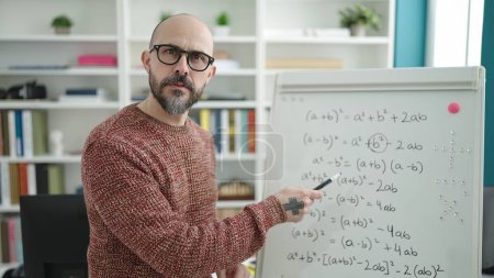 Téléchargez les photos : Jeune homme chauve enseignant les mathématiques sur un tableau magnétique dans une salle de classe universitaire - en image libre de droit