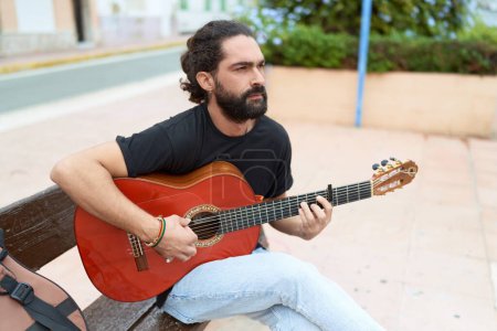 Téléchargez les photos : Young hispanic man musician playing classical guitar sitting on bench at park - en image libre de droit