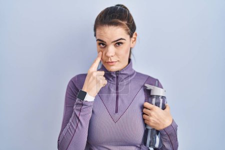 Photo for Beautiful woman wearing sportswear holding water bottle pointing to the eye watching you gesture, suspicious expression - Royalty Free Image