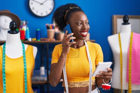 Téléchargez les photos : Femme afro-américaine tailleur parler sur smartphone cahier de lecture au studio de couture - en image libre de droit