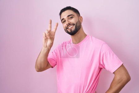Photo for Hispanic young man standing over pink background smiling looking to the camera showing fingers doing victory sign. number two. - Royalty Free Image