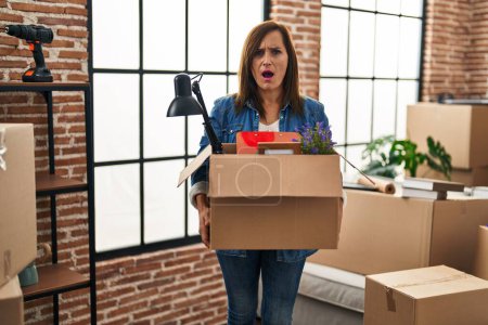Téléchargez les photos : Middle age woman moving to a new home holding cardboard box angry and mad screaming frustrated and furious, shouting with anger. rage and aggressive concept. - en image libre de droit