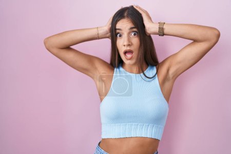 Photo for Young brunette woman standing over pink background crazy and scared with hands on head, afraid and surprised of shock with open mouth - Royalty Free Image