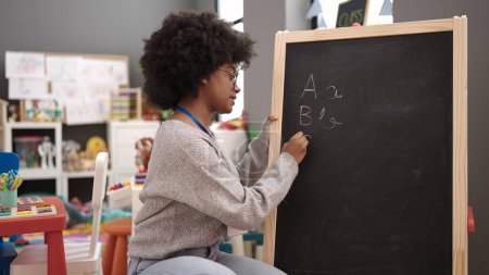 Photo for African american woman teacher writing on blackboard at kindergarten - Royalty Free Image