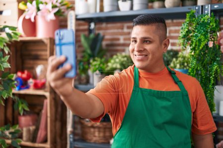 Téléchargez les photos : Jeune fleuriste latin homme faire selfie par smartphone à la boutique de fleurs - en image libre de droit