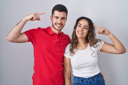 Photo for Young hispanic couple standing over isolated background smiling pointing to head with both hands finger, great idea or thought, good memory - Royalty Free Image