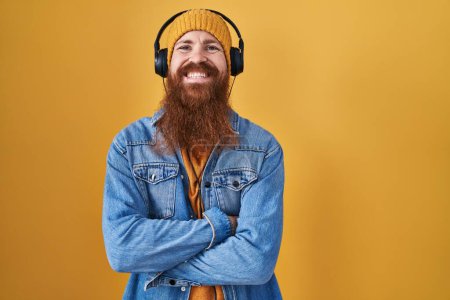 Téléchargez les photos : Homme caucasien à longue barbe écoutant de la musique à l'aide d'écouteurs heureux visage souriant avec les bras croisés regardant la caméra. personne positive. - en image libre de droit