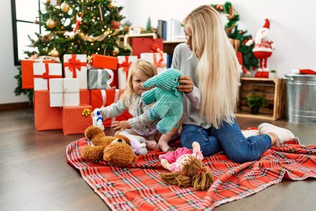 Photo for Mother and daughter playing with toys sitting by christmas tree at home - Royalty Free Image