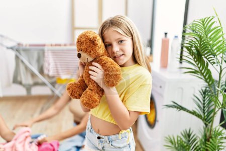 Photo for Mother and daughters holding soft teddy bear washing clothes at laundry room - Royalty Free Image