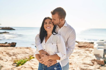 Foto de Hombre y mujer pareja sonriendo feliz abrazándose de pie en la orilla del mar - Imagen libre de derechos