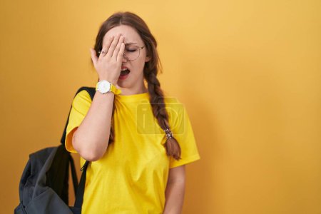 Téléchargez les photos : Young caucasian woman wearing student backpack over yellow background yawning tired covering half face, eye and mouth with hand. face hurts in pain. - en image libre de droit