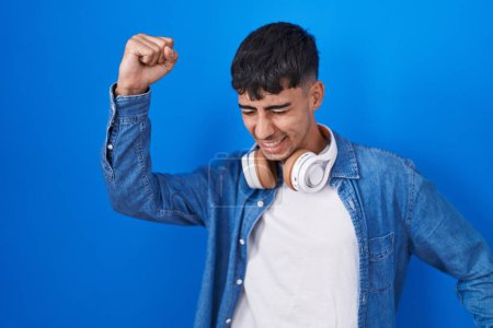 Téléchargez les photos : Jeune homme hispanique debout sur fond bleu dansant heureux et joyeux, souriant décontracté et confiant écoutant de la musique - en image libre de droit
