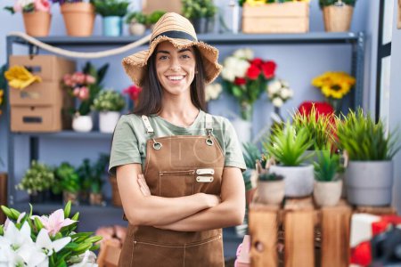 Foto de Joven hermosa florista hispana sonriendo confiada de pie con los brazos cruzados gesto en la tienda de flores - Imagen libre de derechos