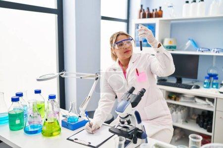 Photo for Young hispanic woman wearing scientist uniform analysing blood at laboratory - Royalty Free Image