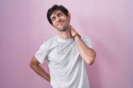 Photo for Young hispanic man standing over pink background suffering of neck ache injury, touching neck with hand, muscular pain - Royalty Free Image
