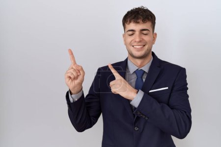 Téléchargez les photos : Jeune homme d'affaires hispanique portant costume et cravate souriant et regardant la caméra pointant avec deux mains et doigts sur le côté. - en image libre de droit