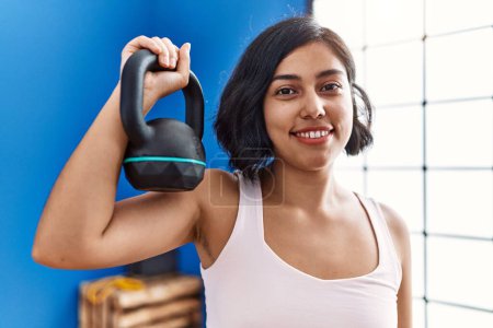 Téléchargez les photos : Jeune femme latine souriant entraînement confiant en utilisant kettlebell au centre sportif - en image libre de droit