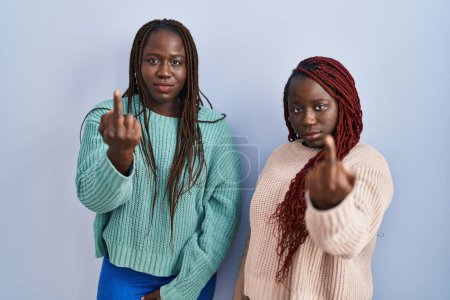Foto de Two african woman standing over blue background showing middle finger, impolite and rude fuck off expression - Imagen libre de derechos