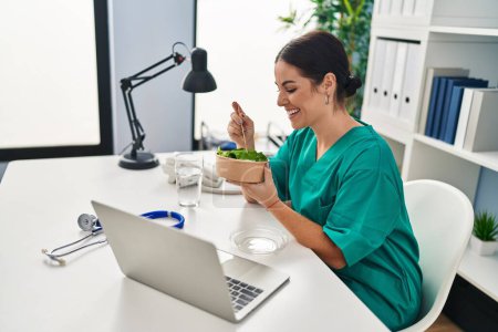 Photo for Young beautiful hispanic woman doctor smiling confident eating salad at clinic - Royalty Free Image