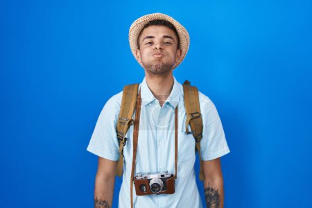 Téléchargez les photos : Brazilian young man holding vintage camera puffing cheeks with funny face. mouth inflated with air, crazy expression. - en image libre de droit