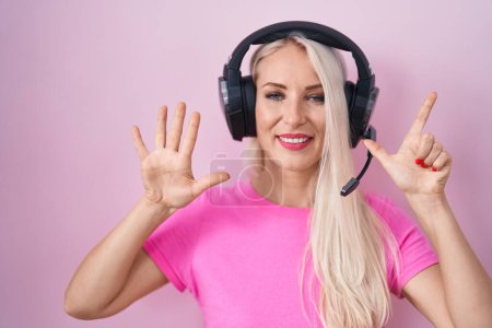 Téléchargez les photos : Femme caucasienne écoutant de la musique à l'aide d'écouteurs montrant et pointant vers le haut avec les doigts numéro sept tout en souriant confiant et heureux. - en image libre de droit