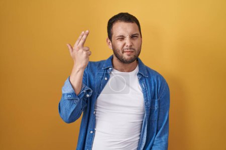 Téléchargez les photos : Homme hispanique debout sur fond jaune tirant et se suicidant pointant la main et les doigts vers la tête comme une arme à feu, geste de suicide. - en image libre de droit