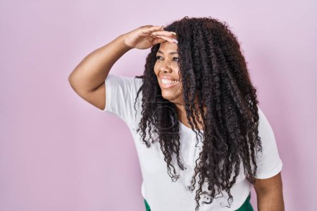 Photo for Plus size hispanic woman standing over pink background very happy and smiling looking far away with hand over head. searching concept. - Royalty Free Image