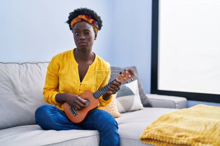 Photo for African young woman playing ukulele at home skeptic and nervous, frowning upset because of problem. negative person. - Royalty Free Image