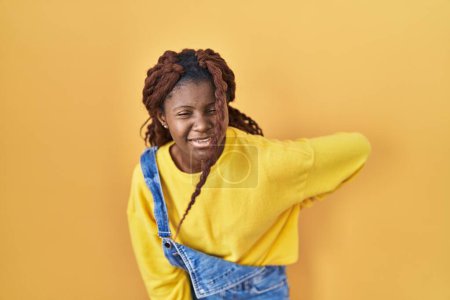 Téléchargez les photos : Femme africaine debout sur fond jaune souffrant de maux de dos, toucher le dos avec la main, douleurs musculaires - en image libre de droit
