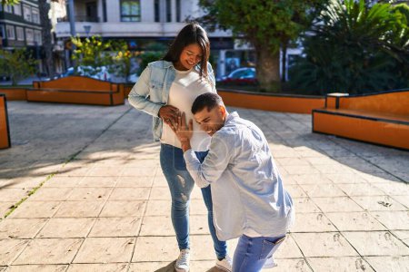 Téléchargez les photos : Jeune couple latin écoutant le son du bébé au parc - en image libre de droit