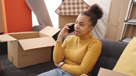 Téléchargez les photos : Jeune femme afro-américaine souriante parlant au téléphone à la nouvelle maison - en image libre de droit