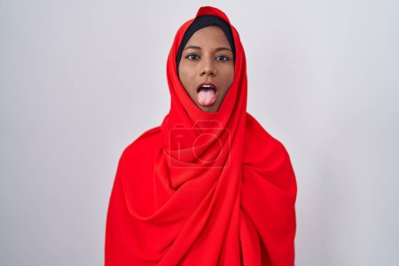 Photo for Young arab woman wearing traditional islamic hijab scarf sticking tongue out happy with funny expression. emotion concept. - Royalty Free Image
