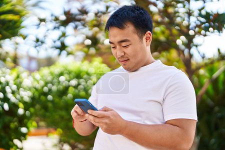 Photo for Young chinese man smiling confident using smartphone at park - Royalty Free Image