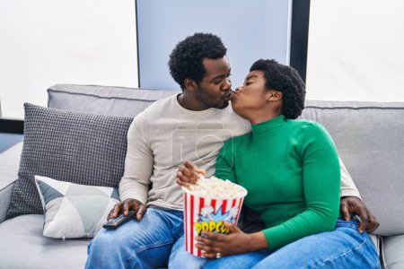 Foto de Africano americano hombre y mujer pareja viendo película comer palomitas de maíz besos en casa - Imagen libre de derechos