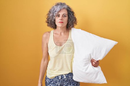 Photo for Middle age woman with grey hair wearing pijama hugging pillow relaxed with serious expression on face. simple and natural looking at the camera. - Royalty Free Image