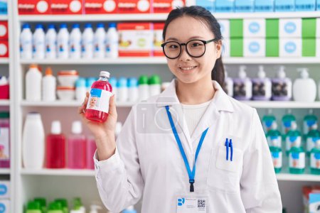 Téléchargez les photos : Jeune pharmacienne chinoise souriante confiante tenant bouteille de médicaments à la pharmacie - en image libre de droit