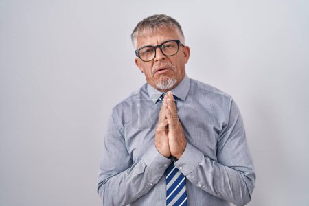 Téléchargez les photos : Hispanic business man with grey hair wearing glasses begging and praying with hands together with hope expression on face very emotional and worried. begging. - en image libre de droit