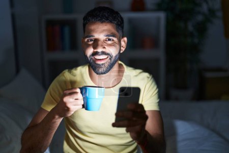 Téléchargez les photos : Jeune homme arabe utilisant smartphone boire du café dans la chambre - en image libre de droit