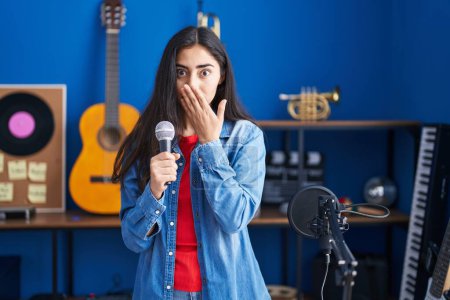Photo for Young teenager girl singing song using microphone covering mouth with hand, shocked and afraid for mistake. surprised expression - Royalty Free Image