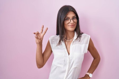 Photo for Brunette young woman standing over pink background wearing glasses smiling looking to the camera showing fingers doing victory sign. number two. - Royalty Free Image